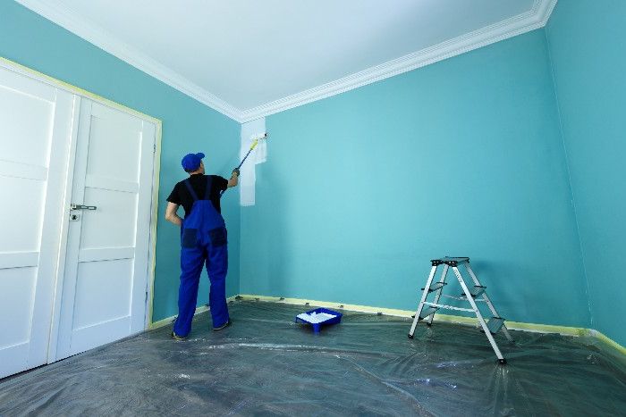 Person streicht Wand mit Farbrolle türkis